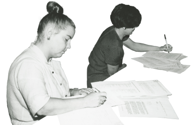 two women writing with a pile of papers